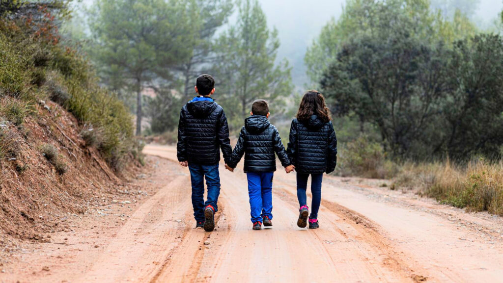 three siblings walking on dirt road